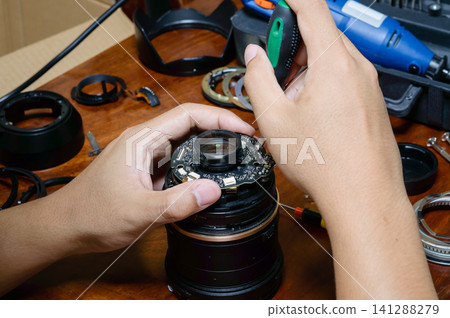 two hands of a man doing work with broken camera lens to fixing it at working table two hands of a man doing work with broken camera lens to fixing it at working table 141288279