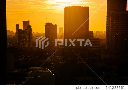 beautiful warm toned color of sky  and the sun on a top of silhouette buildings  in  a city photo with some noise and gain 141288361
