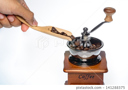 a hand holding handle of the grinding machine coffee with coffee beans from on white background a hand holding handle of the grinding machine coffee with coffee beans from on white background 141288375