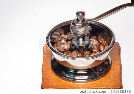 a hand holding handle of the grinding machine coffee with coffee beans from on white background a hand holding handle of the grinding machine coffee with coffee beans from on white background 141288376
