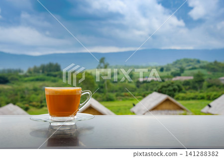 hot Thai's style milk tea in a cup with mountain view when a raining is coming from somewhere faraway 141288382