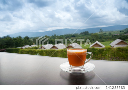 hot Thai's style milk tea in a cup with mountain view when a raining is coming from somewhere faraway hot Thai's style milk tea in a cup with mountain view when a raining is coming from somewhere faraway 141288383