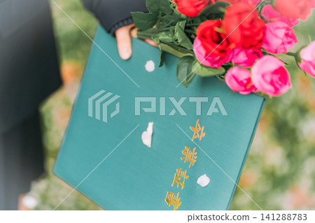 一位高中女生手捧畢業證書和一束玫瑰花，周圍是飄落的櫻花花瓣。 141288783