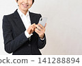 An Asian woman in a suit, smiling and holding a smartphone. 141288894
