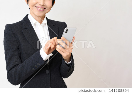 身穿西裝的亞洲女性,面帶微笑,手持智慧型手機。 身穿西裝的亞洲女性,面帶微笑,手持智慧型手機。 141288894