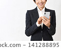 An Asian woman in a suit, smiling and holding a smartphone. 141288895