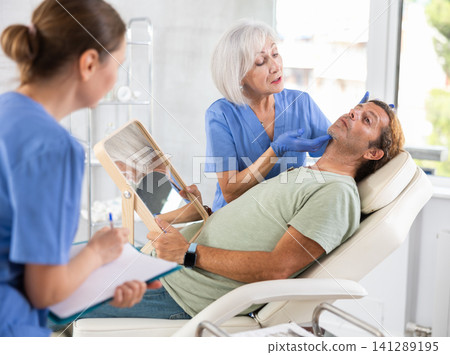 Elderly woman cosmetologist giving professional advice before facial treatments to man Elderly woman cosmetologist giving professional advice before facial treatments to man 141289195