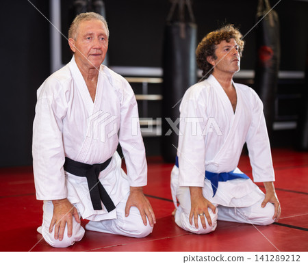 Karate practitioners kneeling in dojo training hall Karate practitioners kneeling in dojo training hall 141289212