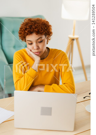 Sleepy sad African American woman sitting at table with laptop. Tired overworked girl lazy to work. Student businesswoman relaxing bored in home office after work on laptop computer Sleepy sad African American woman sitting at table with laptop. Tired overworked girl lazy to work. Student businesswoman relaxing bored in home office after work on laptop computer 141289504
