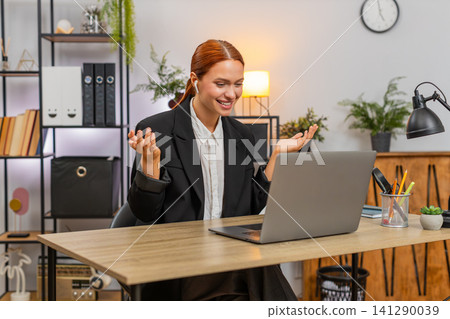 Young businesswoman joins video call on laptop wears earphones waves hi and gestures energetically Young businesswoman joins video call on laptop wears earphones waves hi and gestures energetically 141290039
