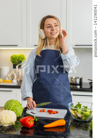 Young woman chopping tomatoes for keto salad while listening to music for meal prep in home kitchen 141290041