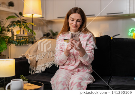 Adult woman online shopping with smartphone credit card at night smiles joy after purchase approval Adult woman online shopping with smartphone credit card at night smiles joy after purchase approval 141290109