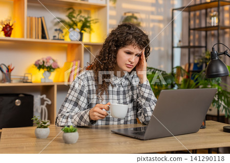 Young woman on home table showing headache from study stress while closing eyes near laptop screen Young woman on home table showing headache from study stress while closing eyes near laptop screen 141290118