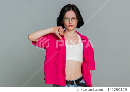 Woman shows thumbs down with serious expression expressing dislike disagreement or disappointment Woman shows thumbs down with serious expression expressing dislike disagreement or disappointment 141290129