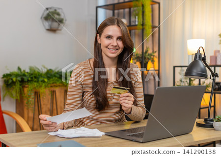 Young woman enters credit card number on laptop pays bills checks totals and presses pay to confirm Young woman enters credit card number on laptop pays bills checks totals and presses pay to confirm 141290138