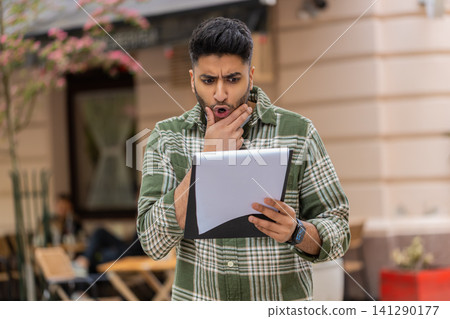 Indian man finding document error walking in city street feeling shocked and disappointed outdoors Indian man finding document error walking in city street feeling shocked and disappointed outdoors 141290177