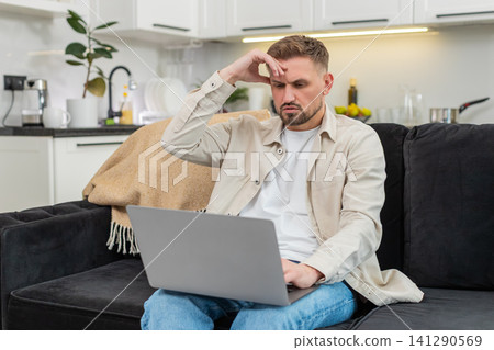 Young man sees defeat on laptop touches forehead sighs and clicks retry after bad news on screen sad Young man sees defeat on laptop touches forehead sighs and clicks retry after bad news on screen sad 141290569