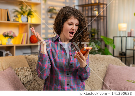 Young woman on home sofa looking at smartphone with wow surprise smile after unexpected sale message 141290628