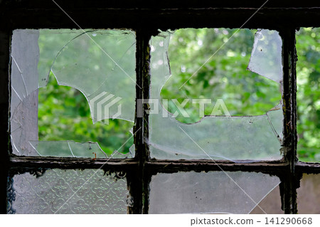 Shattered window panes of an old building looking towards a bright forest and wall Shattered window panes of an old building looking towards a bright forest and wall 141290668