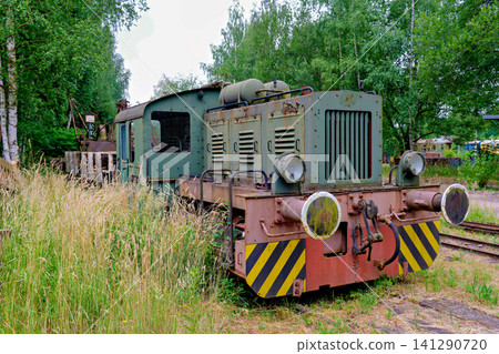 Abandoned vintage narrow gauge train locomotive standing in high green grass next to forest 141290720