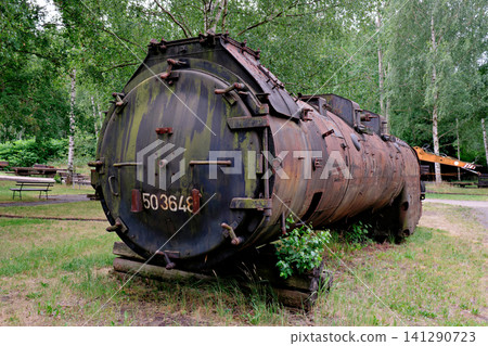 Huge weathered steam locomotive boiler part resting on wooden blocks in a museum park Huge weathered steam locomotive boiler part resting on wooden blocks in a museum park 141290723