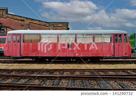 Side view of a retro red railbus carriage on tracks next to an old brick depot building Side view of a retro red railbus carriage on tracks next to an old brick depot building 141290732