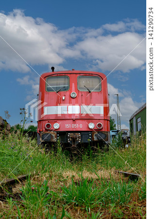 Front view of an old red locomotive parked on overgrown train tracks 141290734