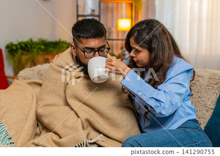 Indian family couple man woman caring for sick ill partner at home, comforting with tea and hugs 141290755