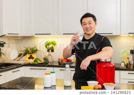 Asian man in kitchen pours glass of milk and drinks protein rich drink for healthy muscle growth fit Asian man in kitchen pours glass of milk and drinks protein rich drink for healthy muscle growth fit 141290823