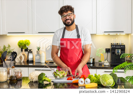 Arabian young adult man cutting tomatoes for salad in kitchen preparing healthy fitness meal at home Arabian young adult man cutting tomatoes for salad in kitchen preparing healthy fitness meal at home 141290824