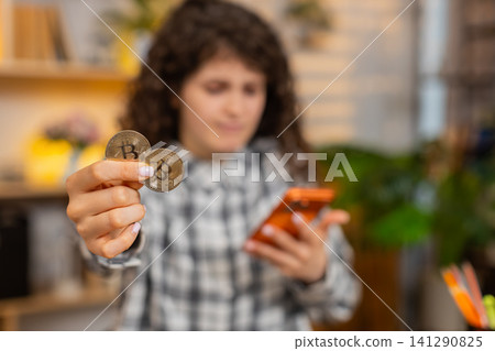 Young woman on home table feeling worried about bitcoin loss while checking smartphone as investor Young woman on home table feeling worried about bitcoin loss while checking smartphone as investor 141290825