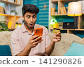 Indian man on home sofa upset after payment decline checking bank card and smartphone in frustration 141290826