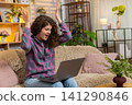 Young woman on home sofa celebrating laptop success after reading job approval results or contract 141290846