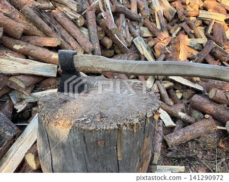 Axe in Chopping Block with Stacked Firewood Background Axe in Chopping Block with Stacked Firewood Background 141290972
