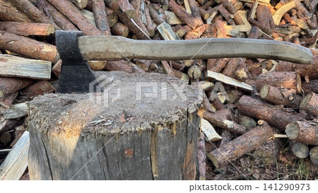 Axe in Chopping Block with Stacked Firewood Logs Background Axe in Chopping Block with Stacked Firewood Logs Background 141290973