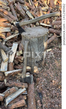 Two Axes Stuck in Wood Block Surrounded by Large Firewood Stack Two Axes Stuck in Wood Block Surrounded by Large Firewood Stack 141290982