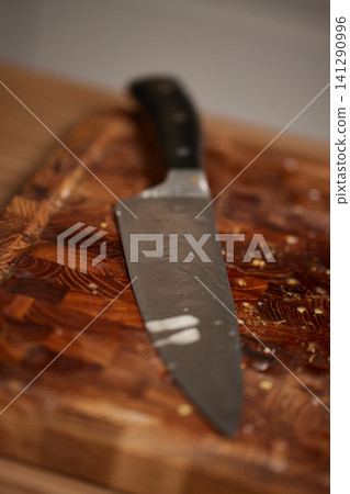 Chef knife with a steel blade resting on a wooden end-grain cutting board, ready for food preparation in a kitchen Chef knife with a steel blade resting on a wooden end-grain cutting board, ready for food preparation in a kitchen 141290996