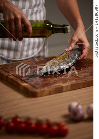 Chef's hands seasoning dorado fish with olive oil on a wooden cutting board, preparing healthy seafood for cooking 141290997