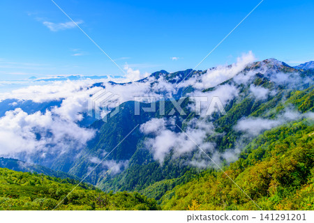 On a clear early autumn day, a view from the climbing route of Mt. Tsubakuro of Mt. Otensho shrouded in clouds, with the silhouettes of Mt. Fuji and the Southern Alps in the distance. On a clear early autumn day, a view from the climbing route of Mt. Tsubakuro of Mt. Otensho shrouded in clouds, with the silhouettes of Mt. Fuji and the Southern Alps in the distance. 141291201