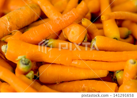 Closeup of a persons hand reaching for fresh, raw carrots in a white plastic crate on a white table Closeup of a persons hand reaching for fresh, raw carrots in a white plastic crate on a white table 141291658