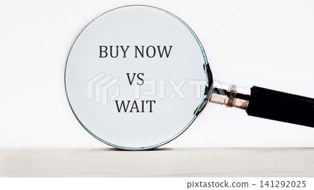 A magnifying glass shows the words buy now and wait, illustrating a choice about when to make a purchase or delay it. This scene represents consumer behavior A magnifying glass shows the words buy now and wait, illustrating a choice about when to make a purchase or delay it. This scene represents consumer behavior 141292025