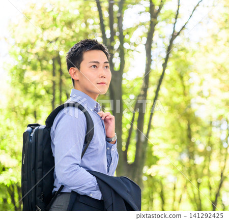 一位商人站在綠樹成蔭的公園裡。 一位商人站在綠樹成蔭的公園裡。 141292425