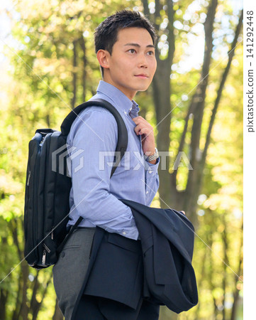 公園裡,一個穿著夾克、背著背包的年輕男子。 公園裡,一個穿著夾克、背著背包的年輕男子。 141292448