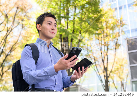 A businessman walks while operating his smartphone. 141292449