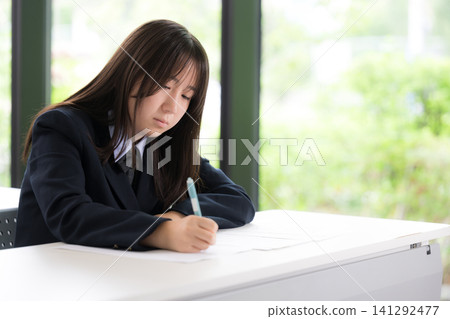 Japanese high school girls diligently studying in a classroom with a beautiful backdrop of fresh greenery; students studying independently for entrance exams and regular tests. Japanese high school girls diligently studying in a classroom with a beautiful backdrop of fresh greenery; students studying independently for entrance exams and regular tests. 141292477