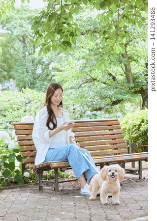 A young woman with her dog is looking at her smartphone on a park bench. A young woman with her dog is looking at her smartphone on a park bench. 141293486
