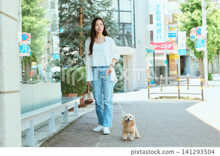 一位女士在城市街道上遛狗。 一位女士在城市街道上遛狗。 141293504