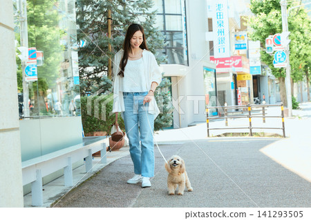 在陽光明媚的日子裡，一位微笑的年輕女子正在遛狗。 141293505