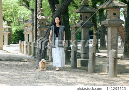 一位女士牽著她的狗沿著通往一座擺滿石燈籠的神社的小路散步。 一位女士牽著她的狗沿著通往一座擺滿石燈籠的神社的小路散步。 141293523
