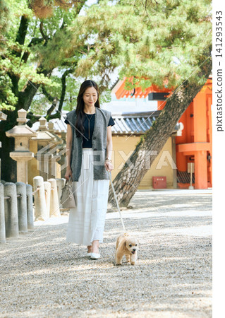 一位面帶微笑的年輕女子在神社內遛狗。 一位面帶微笑的年輕女子在神社內遛狗。 141293543